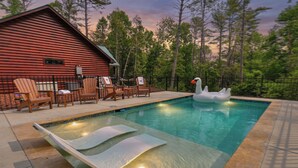 A pool with lounge chairs and a swan float, surrounded by a wooden cabin and trees. - The Liberty Lookout II | Ellijay, Ga (Ellijay)