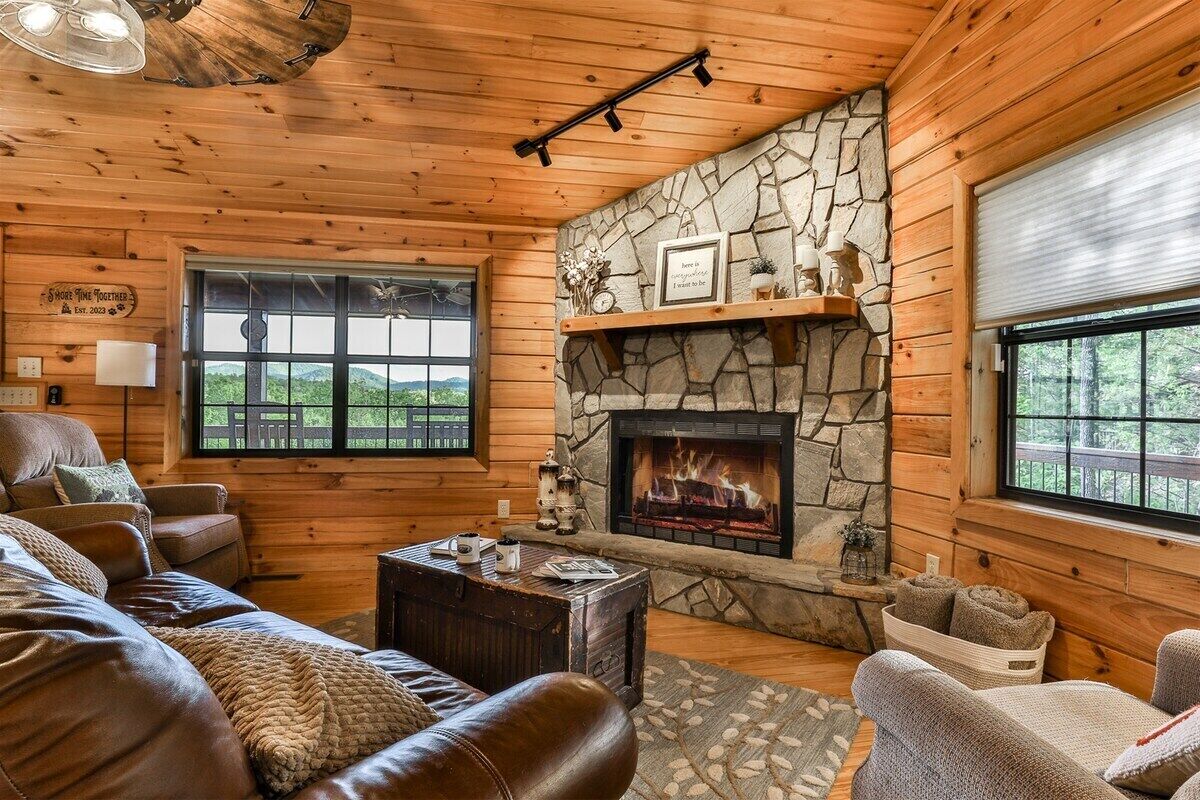Un intérieur de chalet chaleureux avec une cheminée en pierre, des canapés en cuir et de grandes fenêtres.