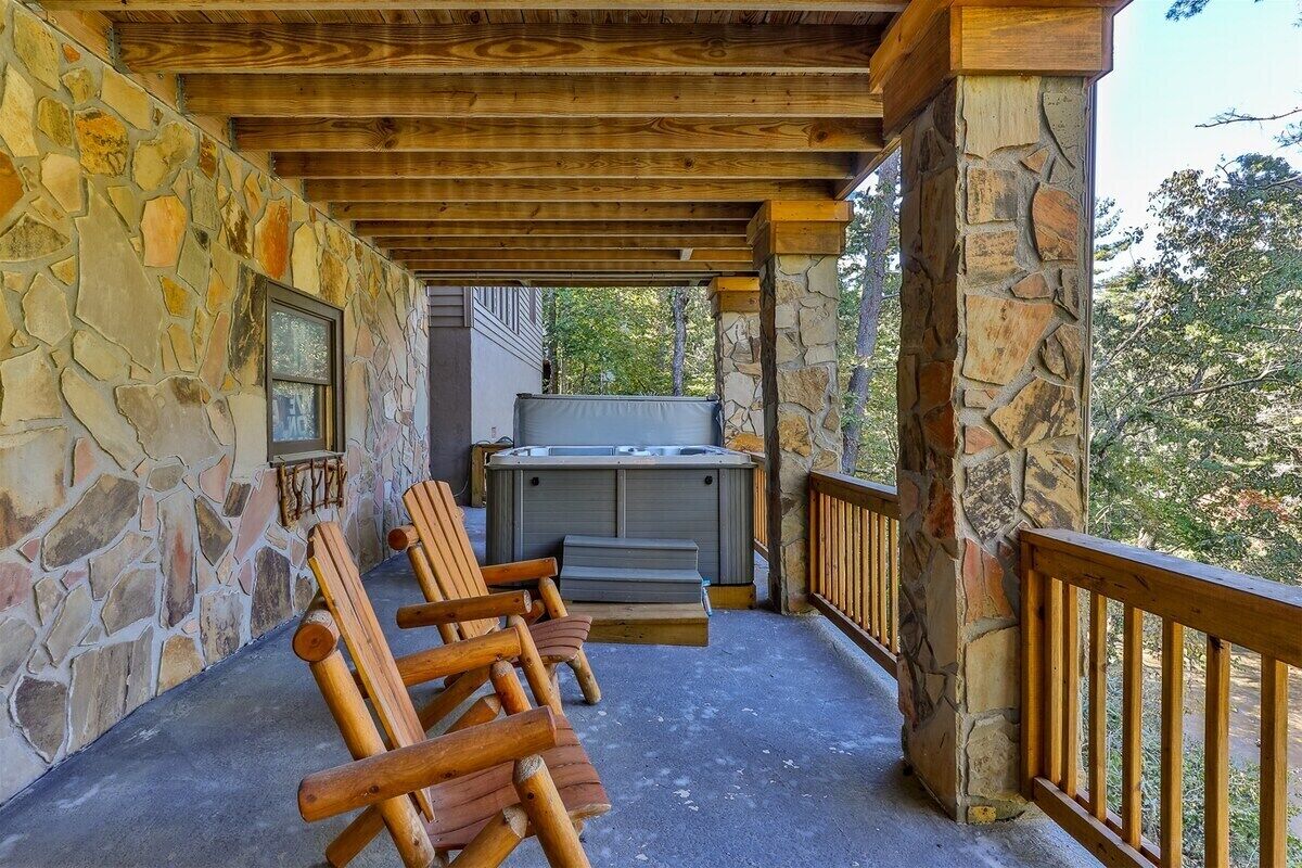 A covered outdoor area with stone walls, wooden benches, and a hot tub.