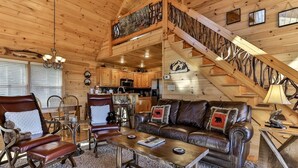 A wooden cabin interior with a living room, dining area, kitchen, and a staircase.