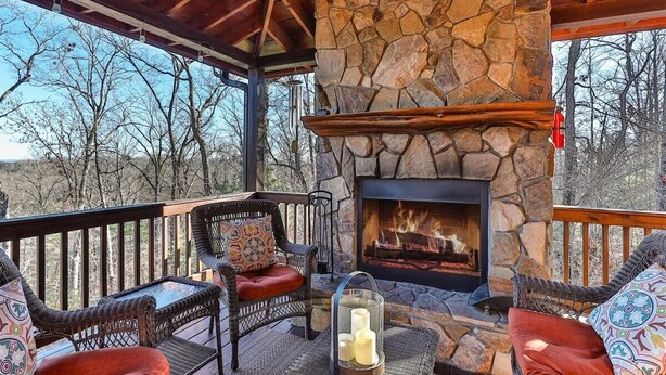 A stone fireplace, wicker furniture, and a view of trees.