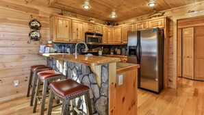 A wooden cabin kitchen with a central island, bar stools, a refrigerator, and a microwave.