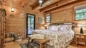 A wooden cabin bedroom with a bed, a ceiling fan, a window, and a door.