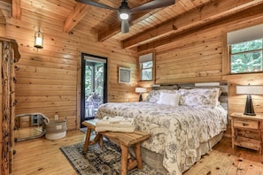 A wooden cabin bedroom with a bed, a ceiling fan, a window, and a door. - A View Above | Ellijay, GA (Ellijay)