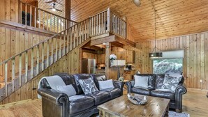 A wooden interior with a staircase, two leather sofas, a wooden coffee table, and a kitchen area.