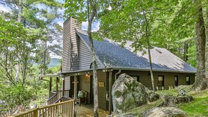 A cabin with a porch, large rocks, and a view of the surrounding forest.
