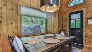 A wooden interior with a dining table, chairs, a large window, and a door with a heart-shaped decoration.