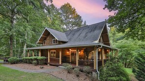 Une cabane en rondins dotée d’une véranda, entourée d’arbres.
