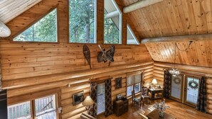 L’intérieur d’une cabane en rondins, avec un plafond haut, de grandes fenêtres, des murs en bois, une tête de cerf fixée au mur et un coin repas.