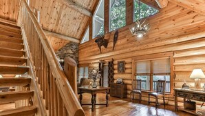 L’intérieur d’une cabane en rondins, avec un escalier en bois, un coin repas et une cheminée.