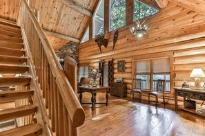 A log cabin interior with a wooden staircase, a dining area, and a fireplace. - Lazy River | Ellijay, GA (Ellijay)
