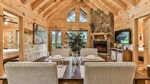 A wooden cabin interior with a dining area, fireplace, and stone wall. - Barn Owl`s Bliss | Cherry Log, GA (Ellijay)