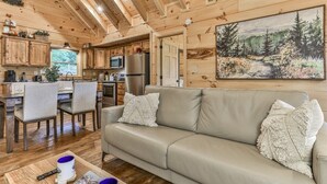A wooden cabin interior with a dining area, kitchen, and a large painting of a forest scene. - Barn Owl`s Bliss | Cherry Log, GA (Ellijay)