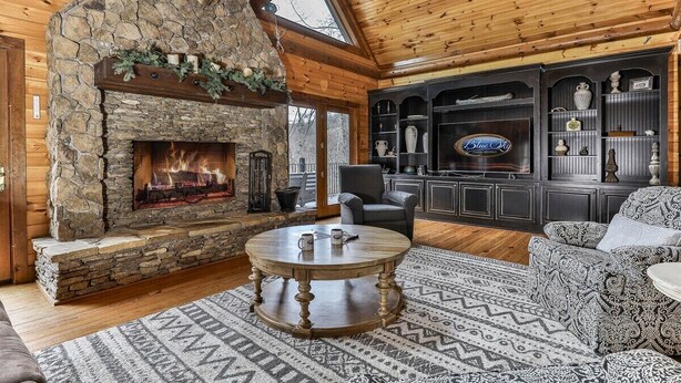 Un salón acogedor con chimenea de piedra, techo de madera y una zona de bar con estanterías y objetos decorativos.