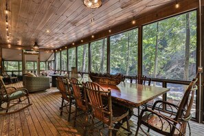 Um deck de madeira com mesa e cadeiras, grandes janelas e vista para a floresta.