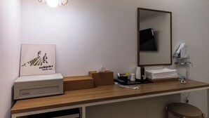 Une chambre d’hôtel avec un comptoir en bois, un miroir, un sèche-cheveux, un téléphone et un tableau encadré au mur.