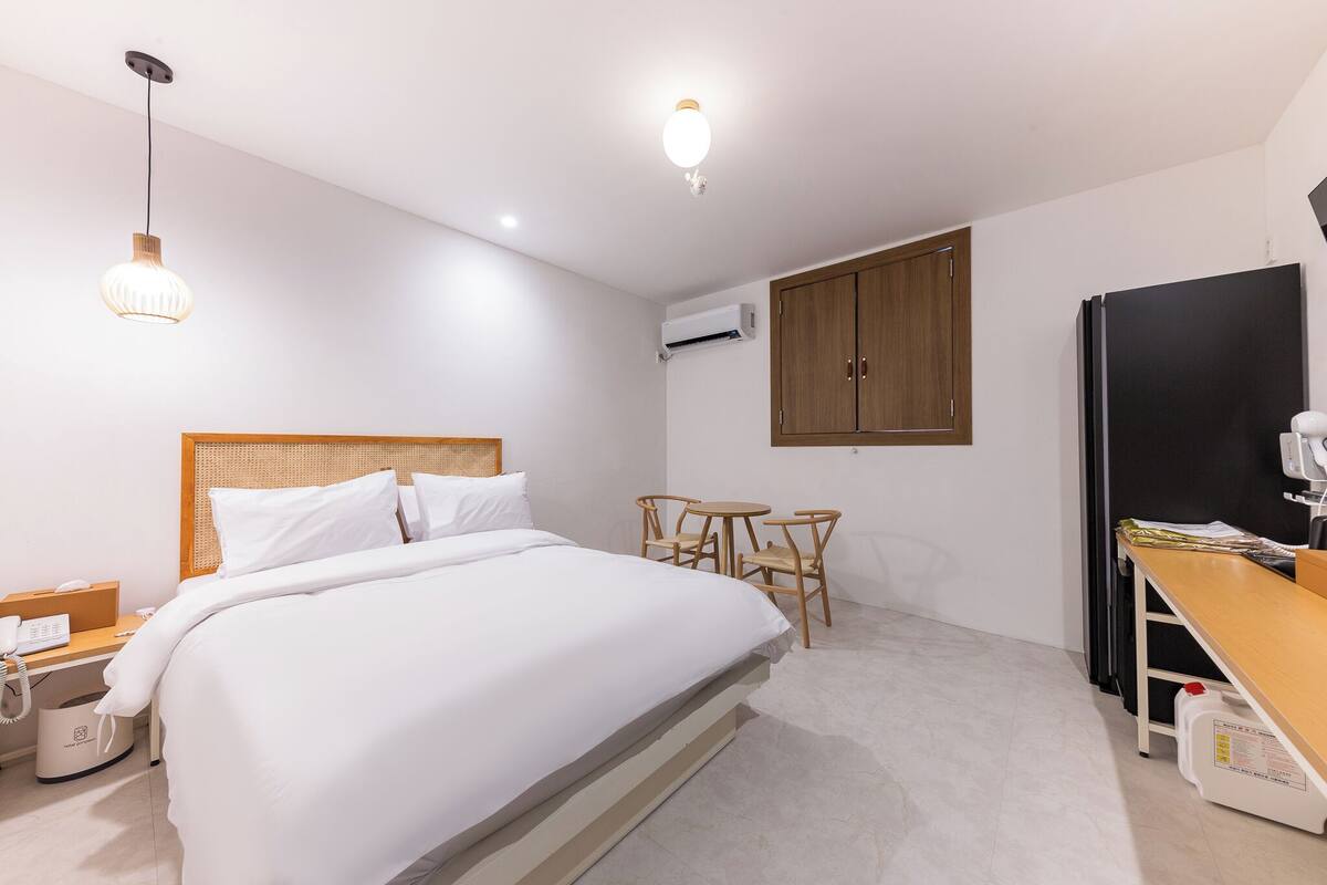 Ein Hotelzimmer mit Bett, Nachttisch, Lampe, Kleiderschrank und Schreibtisch mit Stühlen.