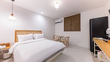 A hotel room with a bed, bedside table, lamp, wardrobe, and a desk with chairs.