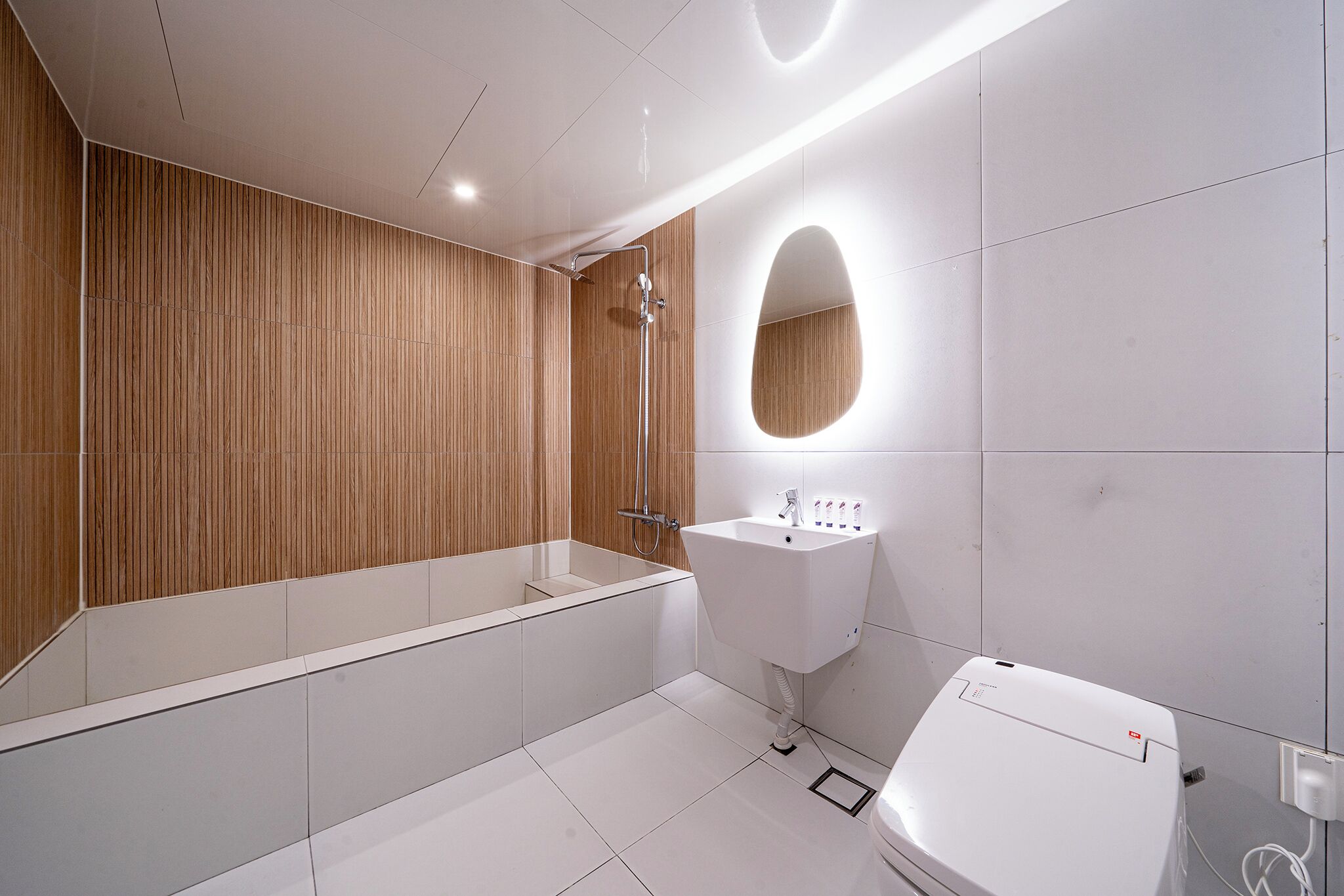 A modern bathroom with a wooden panel wall, a freestanding bathtub, a white sink, and a mirror with an oval frame.