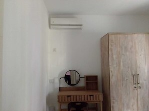 Quarto com escrivaninha de madeira, espelho, guarda-roupa e ar condicionado.