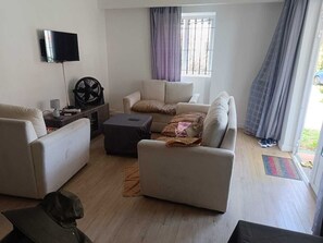 Sala de estar com sofá, televisão, ventilador e janela com cortinas.