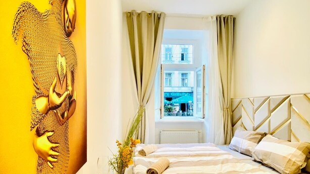 A hotel room with a bed, a desk with a vase of flowers, and a large painting on the wall.