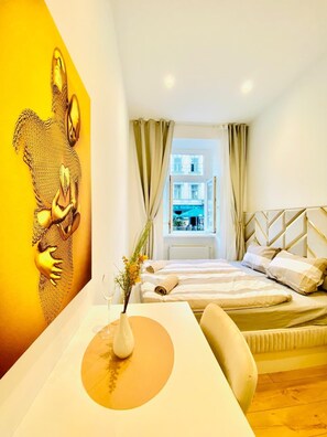 Ein Hotelzimmer mit Bett, Schreibtisch mit Blumenvase und einem großen Gemälde an der Wand.