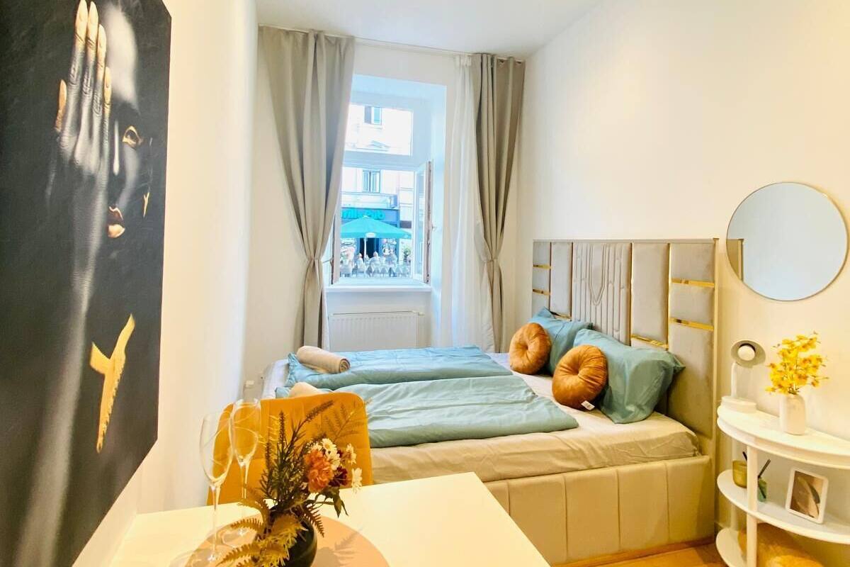 A modern bedroom with a bed, a white table with a vase, and a large abstract painting on the wall.