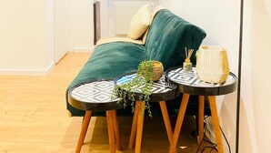 A cozy bedroom with a green sofa, a small round table with a plant, and a floor lamp.