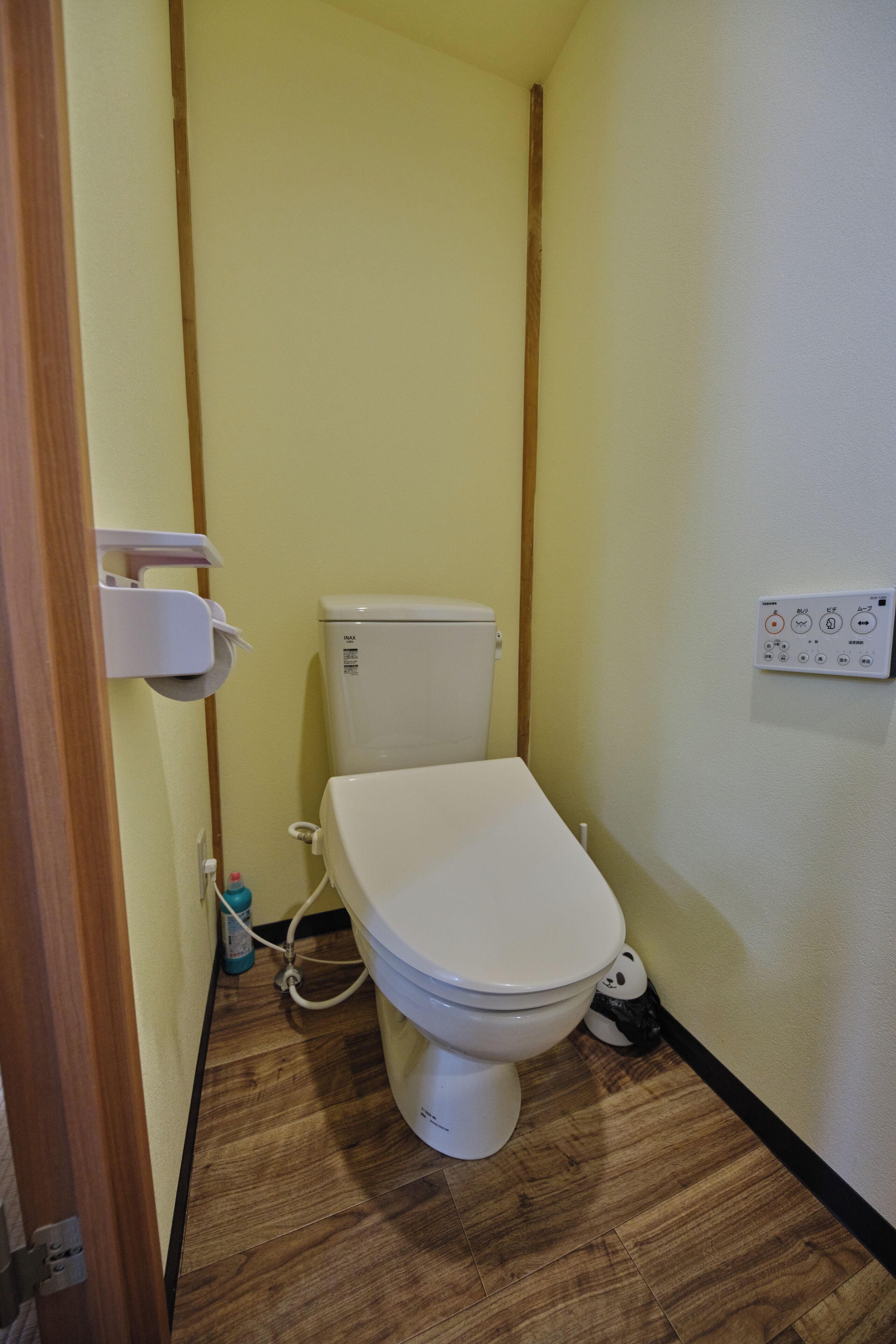 A small bathroom with a toilet, a wall-mounted flush handle, and a wooden floor.