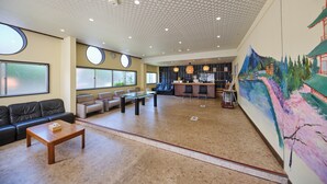 Eine großzügige Lobby mit hoher Decke, einem Empfangsbereich, einer Sitzecke und einem großen Wandgemälde.