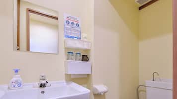 A bathroom with a white sink, mirror, and toilet. There are shelves with toiletries and a small trash bin.