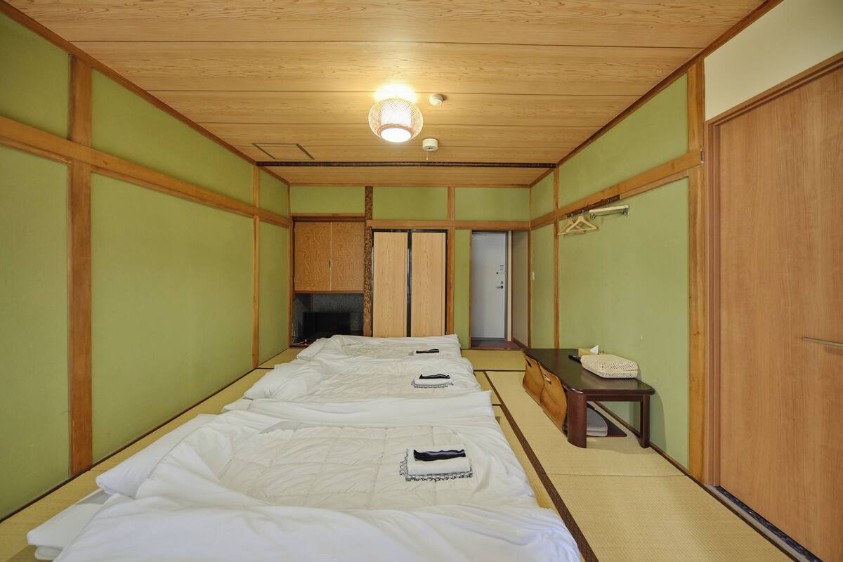 A room with three beds aligned in a row, wooden flooring, and a tatami mat in the center.