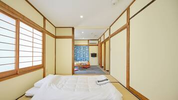 A traditional Japanese-style room with tatami flooring, a low bed, and sliding doors leading to a bathroom.