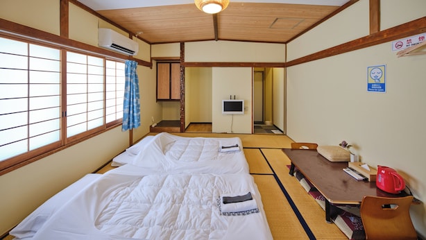 Ein traditioneller japanischer Raum mit Tatami-Boden, Futon-Bett, Holztisch und Fernseher.