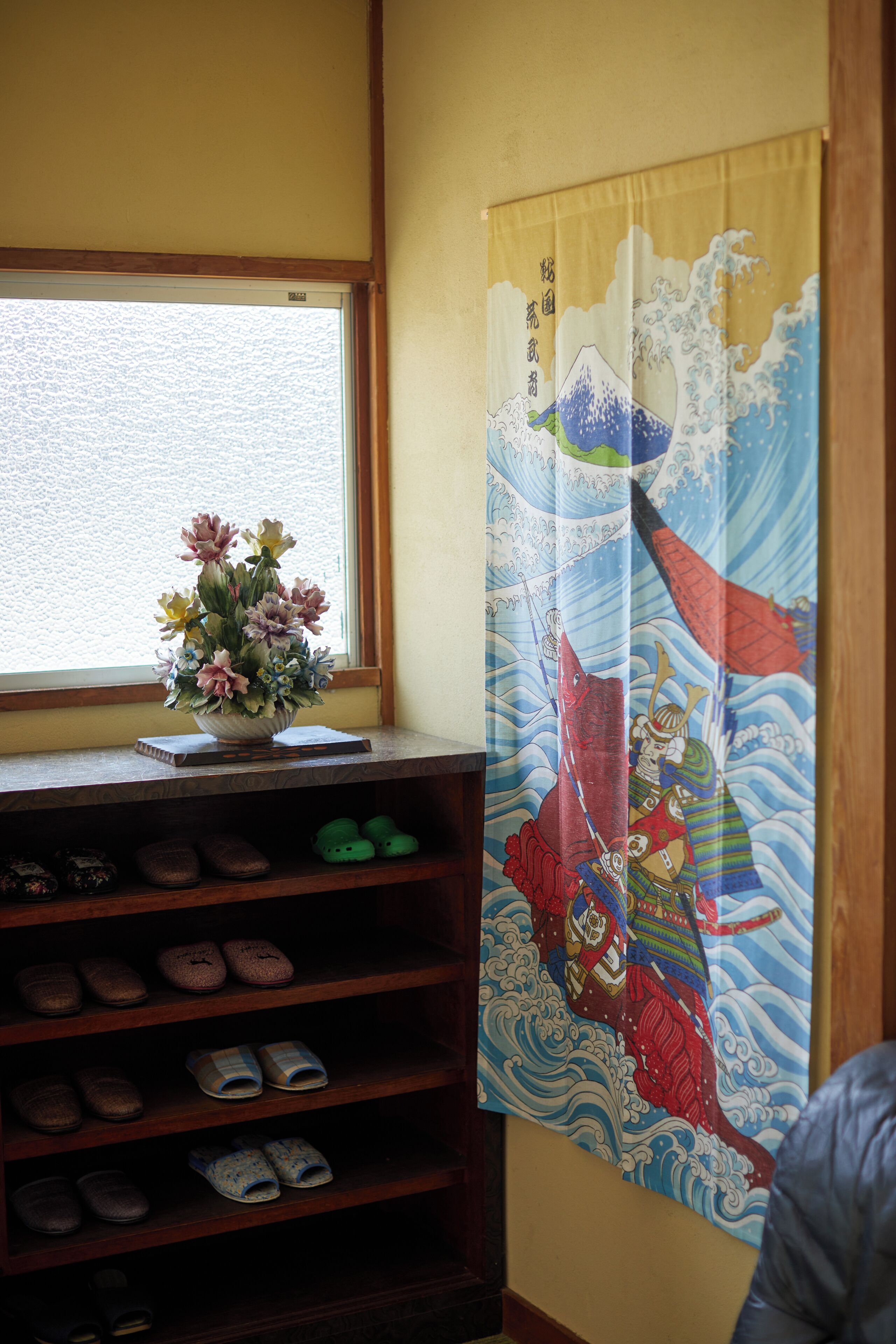 Een kamer met een raam, een bloemenvaas op een plank en een Japanse golfschildering aan de muur.