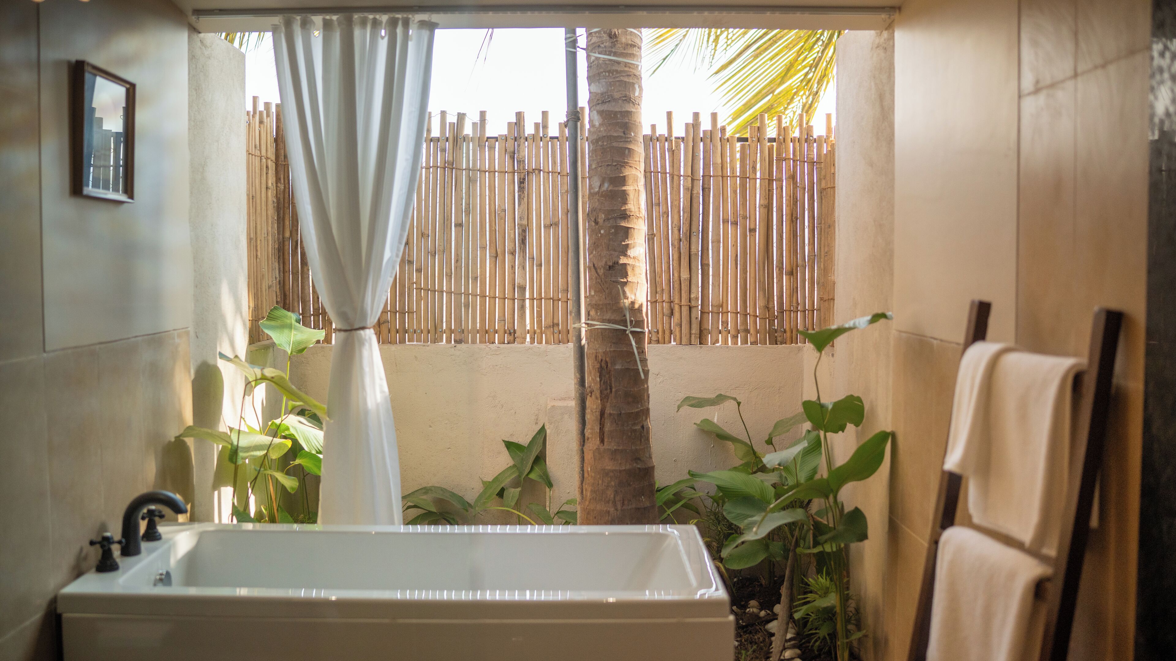 A bathroom with a bathtub, a bamboo fence, and tropical plants.