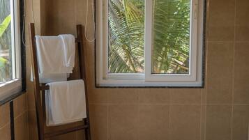 Un baño con ducha, un perchero con toallas y una ventana con vistas a palmeras.