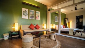 A modern hotel room with a sofa, a glass-top coffee table, and a bed with a large mirror. - Kssema (Mandrem)