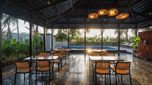 An outdoor dining area with tables and chairs, a pool in the background, and a covered roof structure. - Kssema (Mandrem)