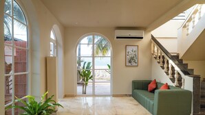 A spacious lobby with a green sofa, a potted plant, and a large arched window offering a view of palm trees. - Kssema (Mandrem)