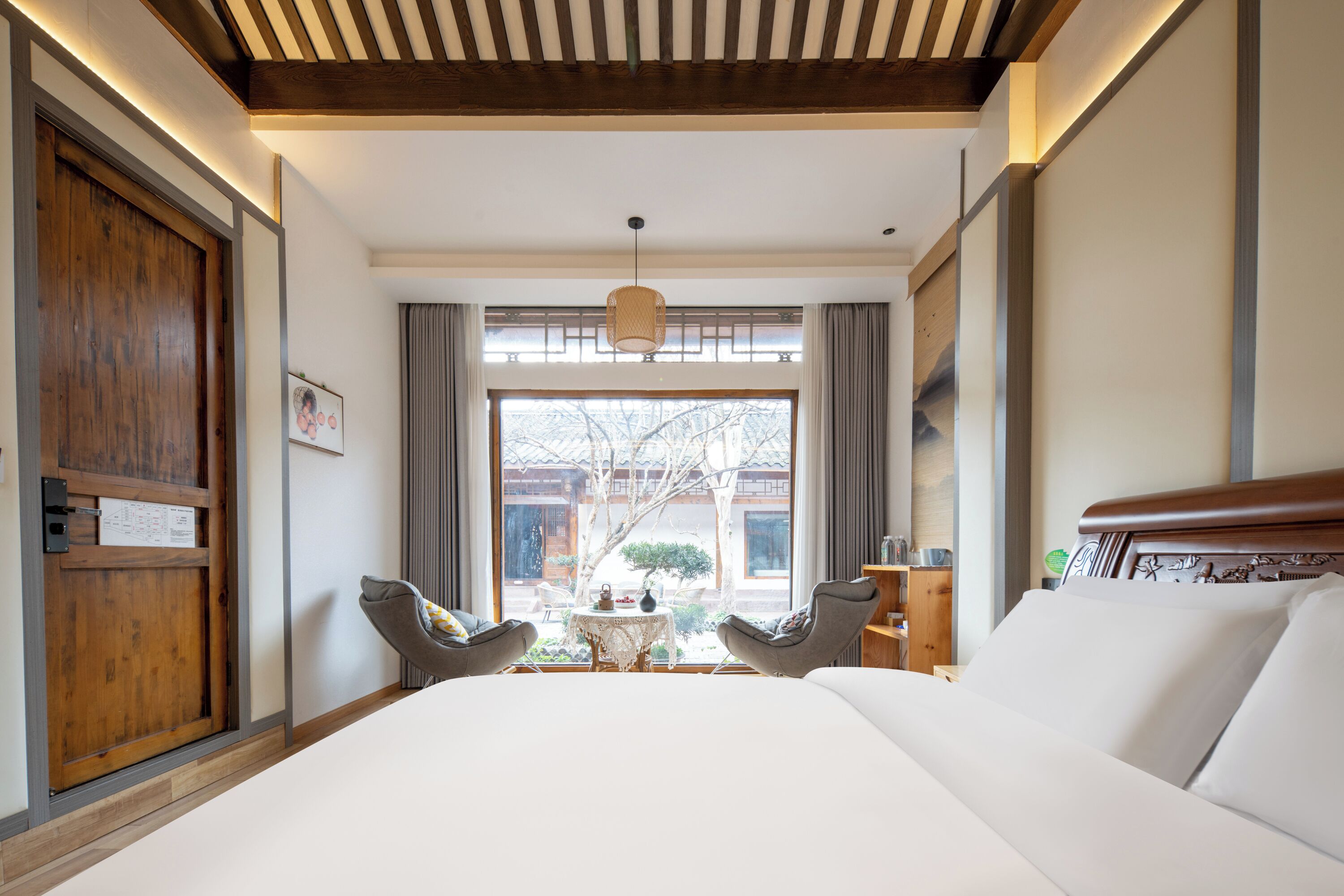 Quarto de hotel com uma cama grande, duas poltronas, uma mesa pequena e vista para o exterior.