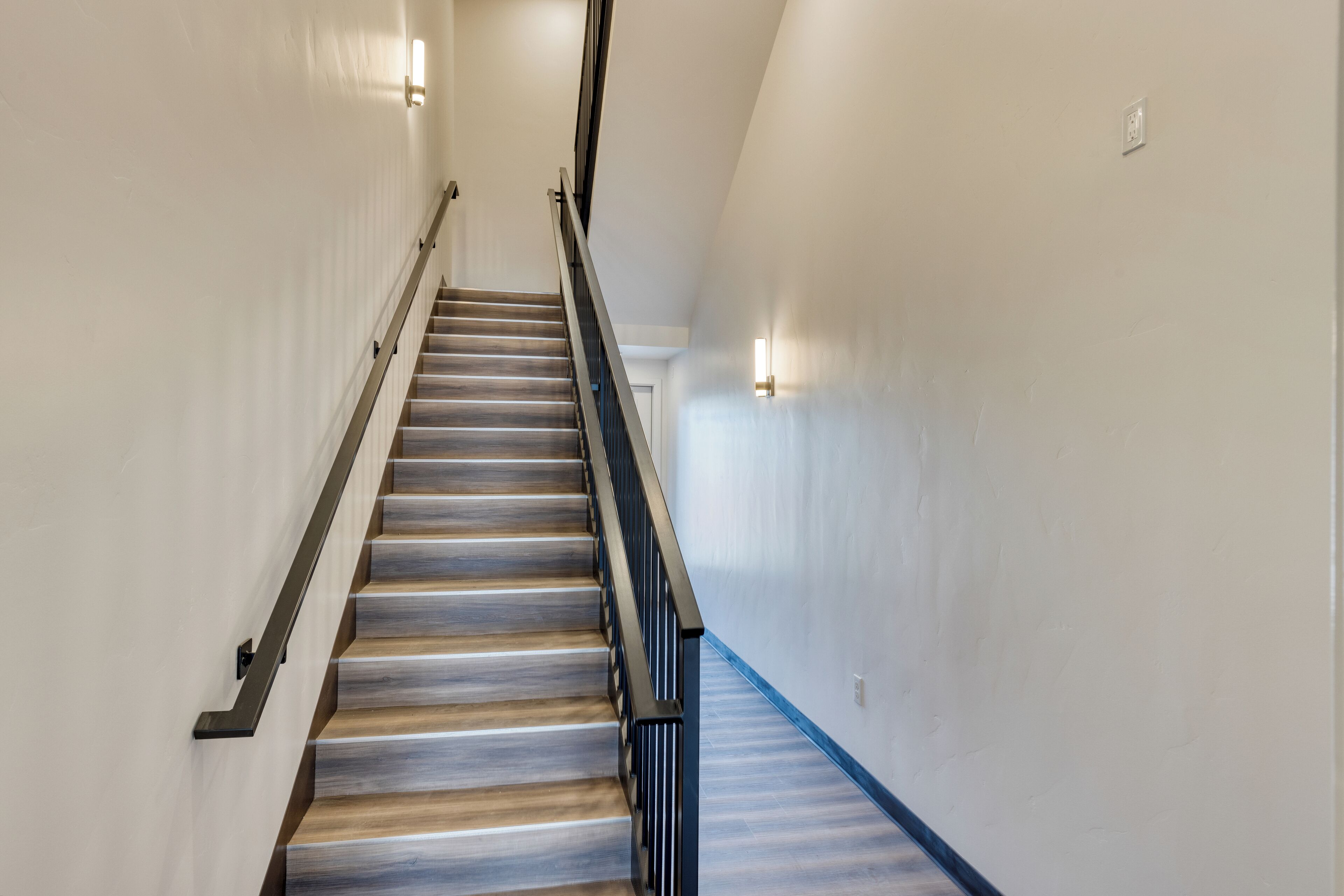 Un escalier avec des marches en bois et des rampes noires, menant à une porte située en haut.