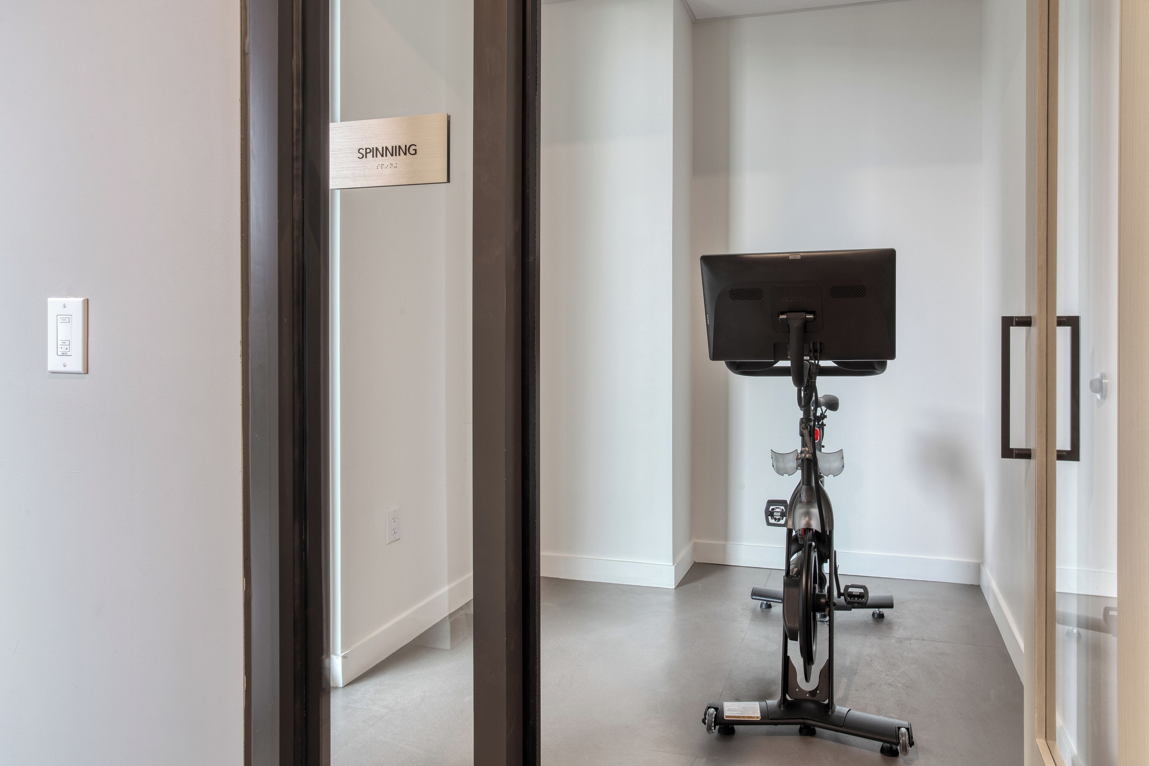 Une pièce comprenant un vélo d’appartement, une pancarte indiquant « SPINNING » et un cadre de porte.