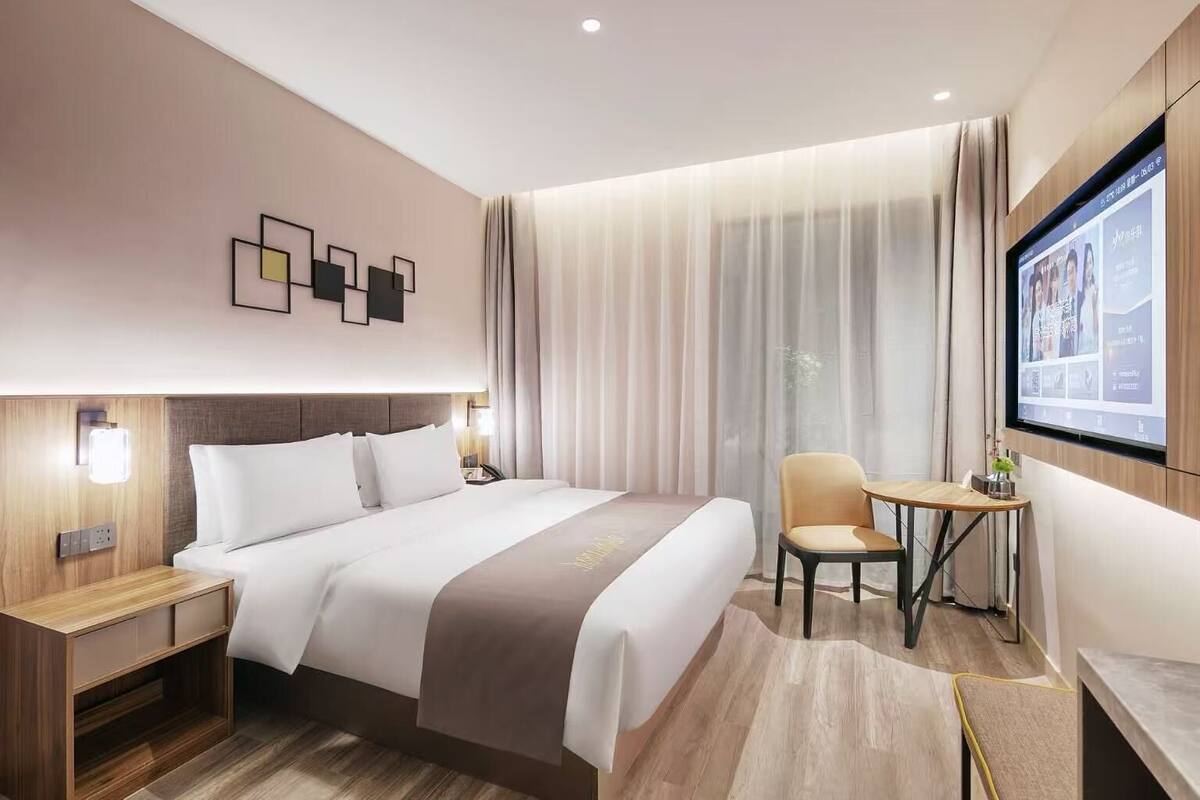 A modern hotel room with a large bed, a desk, and a TV screen.