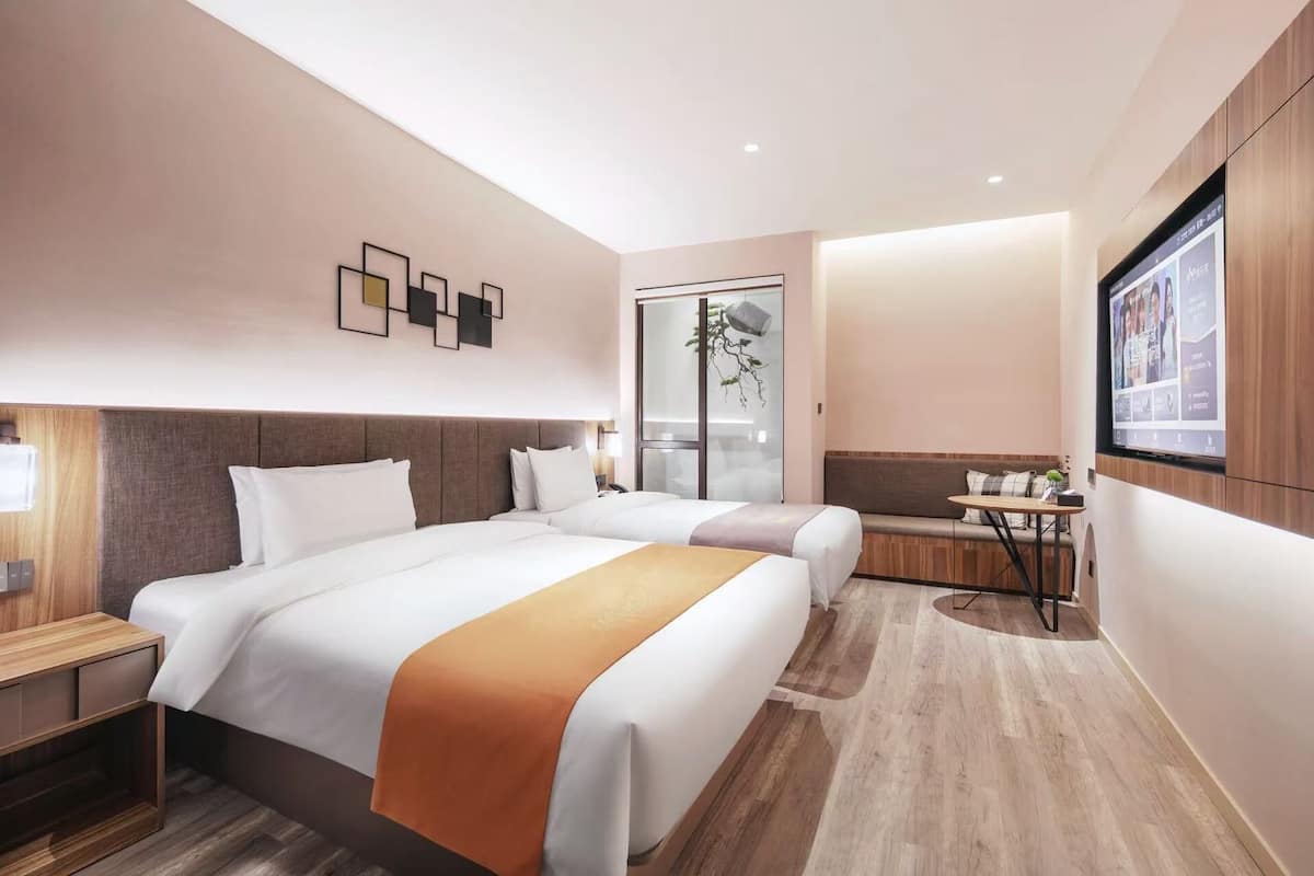 A hotel room with two beds, a small table, a TV, and a sliding door leading to a balcony.