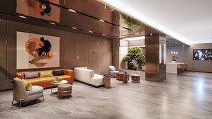 Eine moderne Lobby mit einer Couch, Sesseln, einem kleinen Tisch und einer Rezeption.
