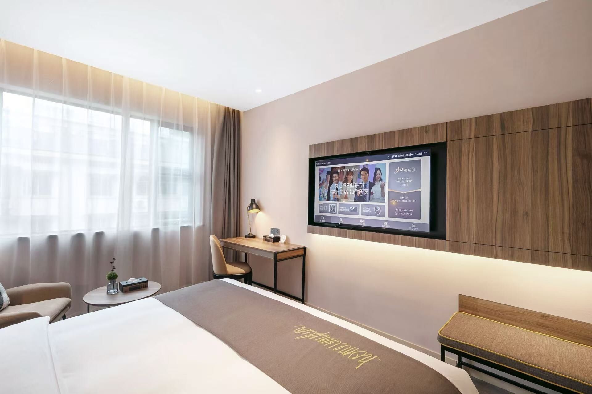 A modern hotel room with a large bed, a desk, and a television mounted on the wall.