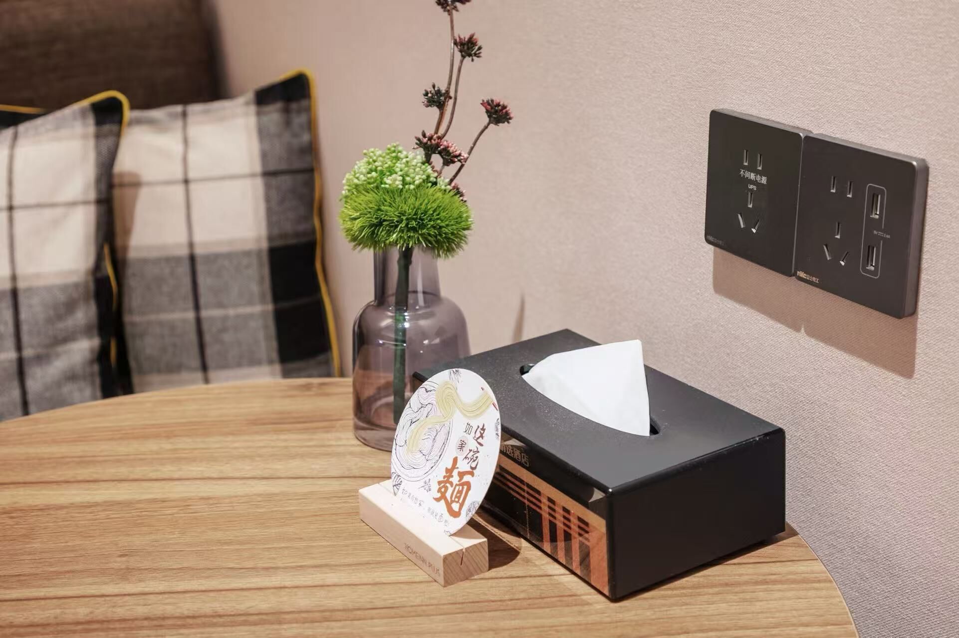 Une table bien rangée, avec un boîte de mouchoirs, un vase décoratif contenant une plante verte et un set de table orné d’un motif.