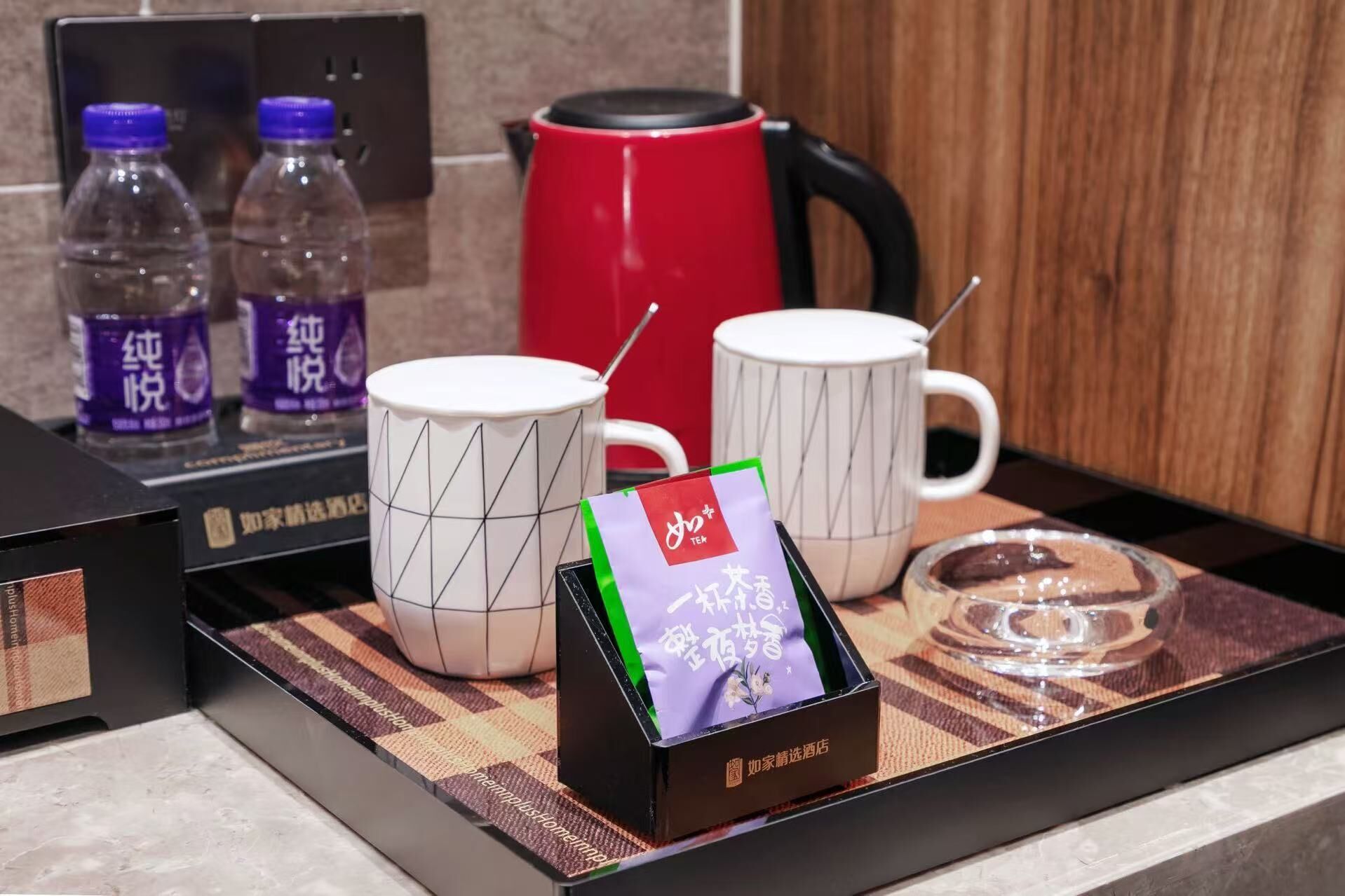 Una bandeja con un juego de té, que incluye una tetera, tazas y una caja de bolsitas de té, sobre un mantel a cuadros.